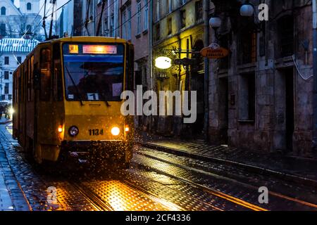 Lviv, Ukraine - 28 décembre 2019 : rue de la vieille ville de Lvov avec neige d'hiver le soir sombre et phares de tram illuminés de couleur jaune Banque D'Images