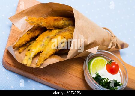 Fried anchois à la pâte servi sur planche à découper en bois avec une sauce au fromage, tomate et citron vert Banque D'Images