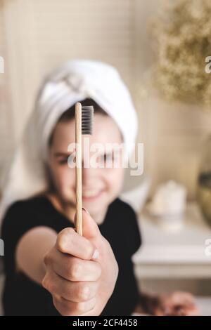 Jeune belle fille avec une serviette sur la tête après la douche, dans la salle de bains tient bambou ECO brosse à dents en face d'elle. Le concept de matin durable Banque D'Images