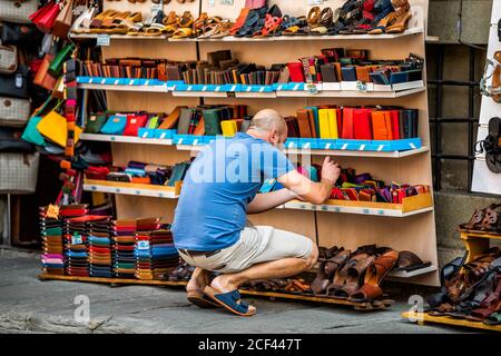 Florence, Italie - 30 août 2018: Beaucoup de produits en cuir exposés dans le magasin de Florence en Toscane avec des gens homme achetant des portefeuilles Banque D'Images