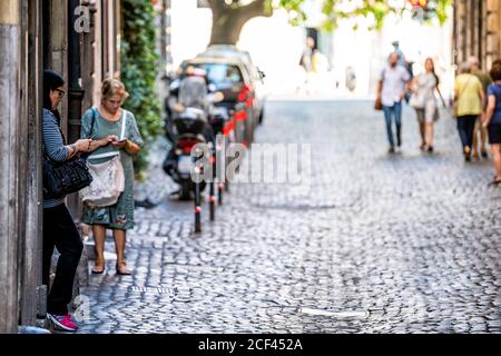 Rome, Italie - 4 septembre 2018: Ville ville rue de route avec des gens touristes debout sur pavés pendu mur regardant les téléphones Banque D'Images