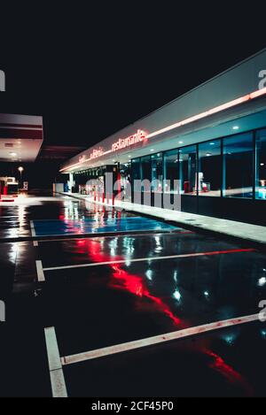 Station-service d'époque déserte avec café et parking à nuit avec lumières réfléchissantes dans l'asphalte humide Banque D'Images