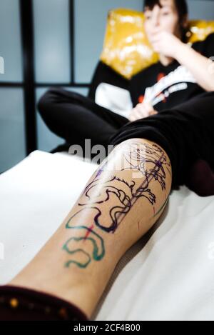 Angle bas de la femme couché sur la table en salon avec transfert de tatouage sur la jambe Banque D'Images