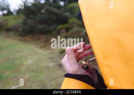 Briquet entre les mains d'un crop-personne en imperméable jaune éclairant cigarette en forêt Banque D'Images