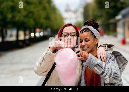 Des amis multiraciaux enthousiastes qui s'embrasent et mangent des bonbons en coton dans le parc Banque D'Images