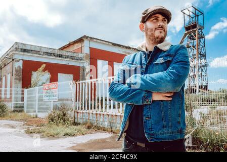 Un homme à barbe en costume décontracté et qui regarde loin à l'extérieur, bâtiment industriel abandonné Banque D'Images