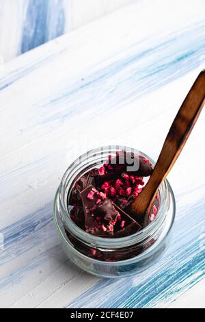 Des morceaux de chocolat au lait savoureux faits maison avec marmelade dans un pot en verre avec une cuillère en bois sur une table en bois Banque D'Images