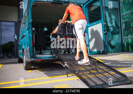 Femme en fauteuil roulant utilisant une rampe de véhicule. Transport accessible avec chauffeur assistant. Banque D'Images