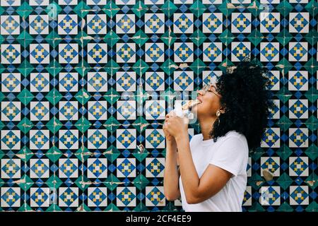 Belle jeune femme en t-shirt blanc debout près d'un mur de carreaux colorés, gaufré mordant Banque D'Images