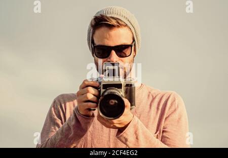 Le photojournaliste concept. Journaliste de prendre photo. Hipster Des réglages manuels. Billet d'un blogueur. Photographe professionnel. Photographe guy beau appareil photo rétro. Guy photographe en plein air fond de ciel. Banque D'Images