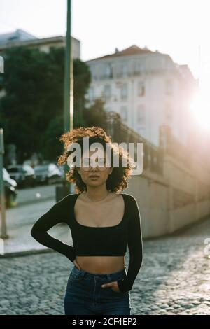 Femme afro-américaine à la mode, en noir, debout sur le trottoir et regardant la caméra Banque D'Images