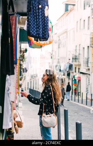 Vue latérale d'une jeune femme regardant des vêtements colorés à vendre se trouvant dans la cabine de la rue de la vieille ville Banque D'Images