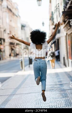 Vue arrière d'une femme ethnique heureuse dans une tenue tendance sautant pour la joie le jour d'été Banque D'Images