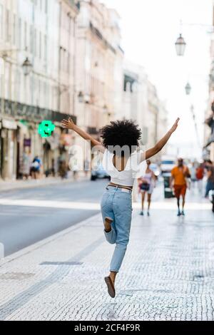 Vue arrière d'une femme ethnique heureuse dans une tenue tendance sautant pour la joie le jour d'été Banque D'Images