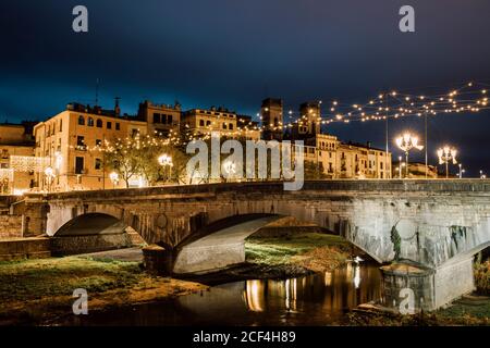 Paysage majestueux de l'ancien pont lumineux au-dessus de la rivière reflétant la lumière de la ville à Gérone, Catalogne, Espagne Banque D'Images