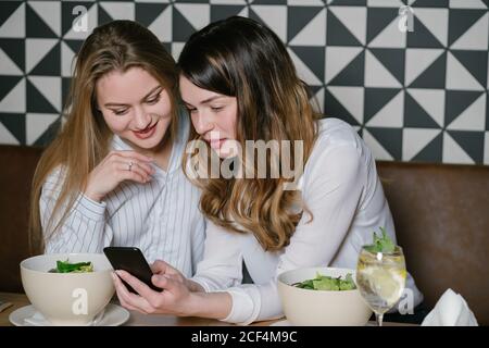 Des femmes élégantes amis utilisant le téléphone tout en étant assis à la table de restaurant pendant le déjeuner Banque D'Images