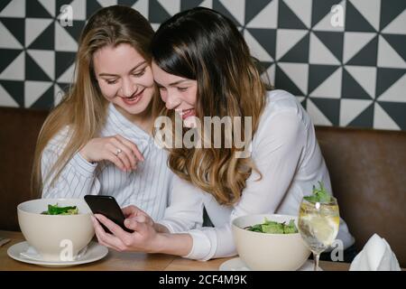 Des femmes élégantes amis utilisant le téléphone tout en étant assis à la table de restaurant pendant le déjeuner Banque D'Images