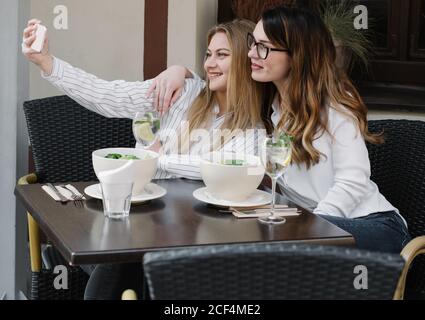 Deux amies élégantes souriant et posant pour le selfie asseyez-vous à table dans un restaurant confortable Banque D'Images