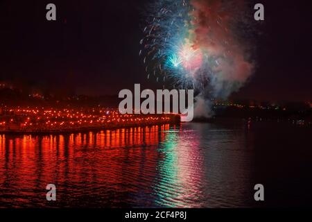 Feux d'artifice multicolores dans la ville la nuit avec reflet de l'eau. Célébration. Arrière-plan abstrait des vacances. Banque D'Images
