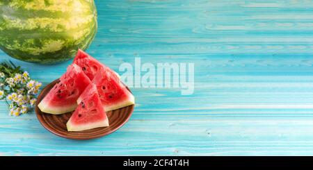 Quatre tranches de pastèque fraîche mûre sont dans une assiette en argile sur une table en bois bleu. Theres un melon d'eau entier dans le fond. Chamomiles. Copier l'espace. Banque D'Images