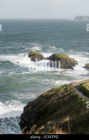 Vue aérienne d'une personne méconnaissable marchant sur une route rurale étroite courir le long d'un terrain vert le jour ensoleillé du printemps sur la côte En Irlande du Nord Banque D'Images