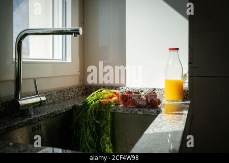 Légumes et bouteille de jus d'orange près d'un évier de cuisine à la maison Banque D'Images