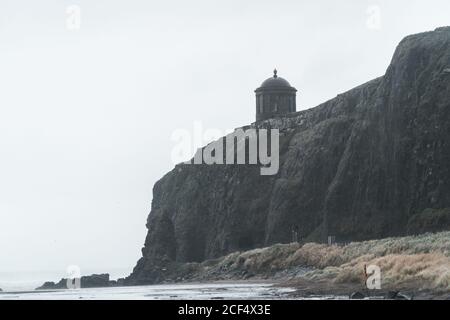 Paysage pittoresque avec le temple de Mussenden situé sur la falaise en pierre à Le littoral de l'Irlande du Nord et les vagues de la mer de tempête s'écrasant contre les rochers avec ciel gris nuageux en arrière-plan Banque D'Images