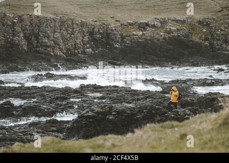 Homme voyageur debout sur le rocher avec l'appareil photo sur trépied et Prise de vue d'un paysage marin par une sombre journée dans le nord Littoral irlandais Banque D'Images