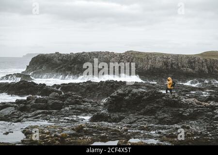 Homme voyageur debout sur le rocher avec l'appareil photo sur trépied et Prise de vue d'un paysage marin par une sombre journée dans le nord Littoral irlandais Banque D'Images