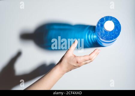 Récolte personne sans visage qui atteint la main pour le plastique et la transparence bouteille de liquide bleu avec bulles situées sur la surface blanche Banque D'Images