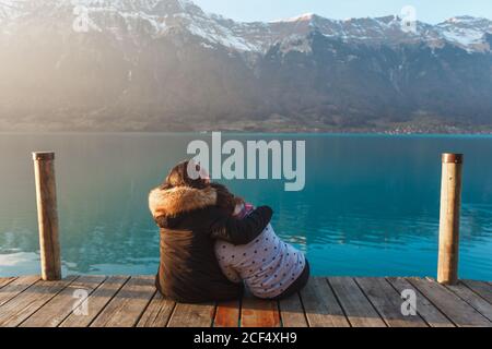 Vue arrière de femmes embrassant assis sur la jetée en bois au-dessus Lac turquoise dans les montagnes enneigées de la Suisse Banque D'Images