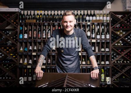 Portrait d'un sommelier debout dans une cave à vin tenant un verre de vin et montrant le pouce vers le haut, pendant une dégustation Banque D'Images