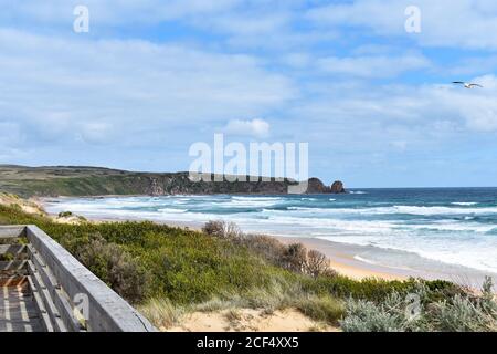 Une petite section de la promenade en bois sur la plage de Cape Woolamai. L'herbe pousse le long des bords de la plage de sable doré alors que la vague s'effondrent de la mer bleue. Banque D'Images