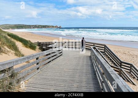 Un visiteur marche le long de la promenade jusqu'à la plage de surf de Cape Wolamai sur Phillip Island, en Australie. Sable doré et eau bleue du détroit de Bass. Banque D'Images