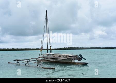 Un petit bateau de pêche local ancré dans les eaux tropicales bleu clair au large de la plage de Vao sur l'île des pins, en Nouvelle-Calédonie, par une journée nuageux et couvert. Banque D'Images