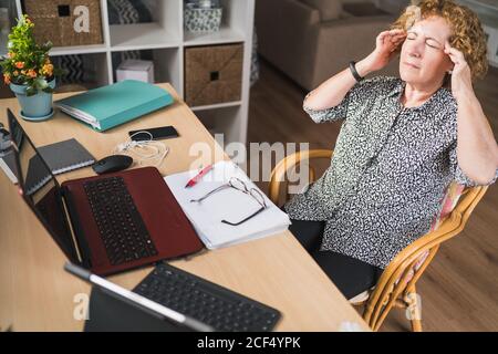 De la vue ci-dessus de la concentration des femmes freelance temples frottant tout en restant sur la chaise avec les yeux fermés pendant le travail avec documents et gadgets Banque D'Images