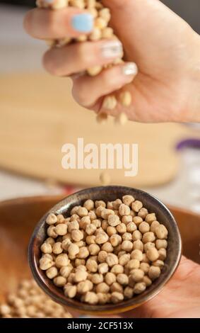 D'en haut anonyme femelle portant une poignée de pois chiches frais plus bol et démonstration du grain à l'appareil photo Banque D'Images