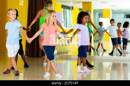 Groupe d'enfants avec leur professeur tenant les mains et dansant en cercle dans l'école de danse Banque D'Images