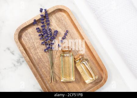 Vue de dessus fleur de lavande et son huile essentielle sur un bouteille sur une table en marbre sur un plateau en bois Banque D'Images