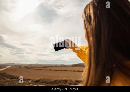 Vue arrière d'une femme anonyme en tenue élégante et décontractée prenant selfie sur téléphone mobile dans le désert à Bardenas Reales, Navarre, Espagne Banque D'Images