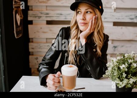 Belle femme blonde à cheveux longs et tendance, buvant un verre de délicieux café mousseux Banque D'Images