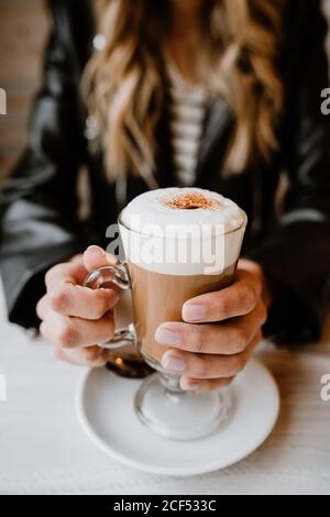 Courte inreconnaissable tendance belle femme blonde boire d'un verre de délicieux café mousseux Banque D'Images