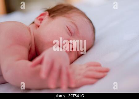 Bébé calme et mignon avec les yeux fermés recouverts d'une couverture de repos dans le lit contre l'intérieur flou de la chambre claire Banque D'Images