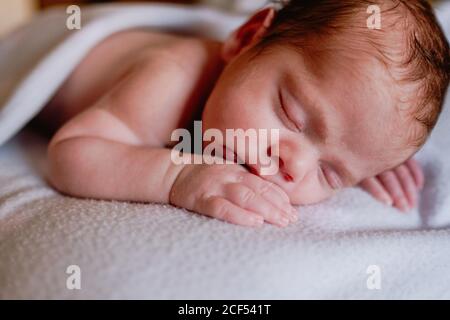 Bébé calme et mignon avec les yeux fermés recouverts d'une couverture de repos dans le lit contre l'intérieur flou de la chambre claire Banque D'Images