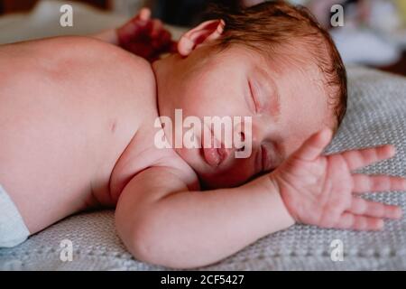 Bébé calme et mignon avec les yeux fermés recouverts d'une couverture de repos dans le lit contre l'intérieur flou de la chambre claire Banque D'Images