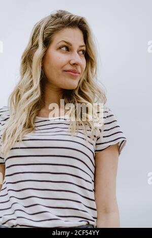 Jeune femme caucasienne décontractée avec cheveux longs blonds regardant loin sur fond neutre Banque D'Images