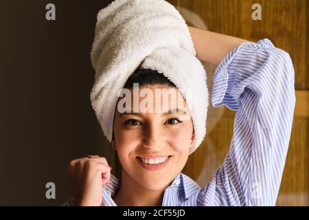 Femme souriante avec une serviette en tissu éponge blanche sur la tête penchée à portée de main et en regardant l'appareil photo à plat sous le soleil jour Banque D'Images