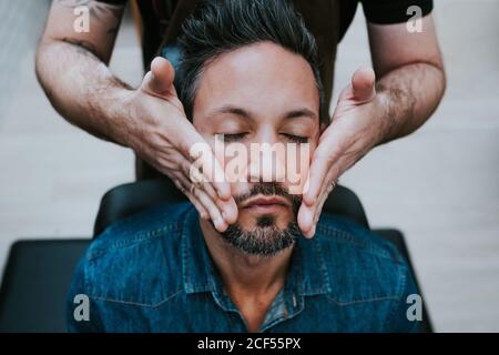 Crop barber faisant un massage du visage à un homme élégant avec beau les yeux fermés sont assis sur la chaise Banque D'Images