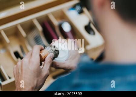 De dessus, crop mâle avec la brosse et la crème de rasage à proximité équipements en barbershop sur fond flou Banque D'Images