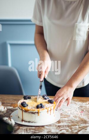 Les mains de la femme coupent le gâteau avec de la crème rose sur le bleu arrière-plan en bois Banque D'Images